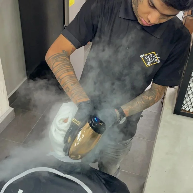 Barbero profesional utilizando vapor para desinfectar toallas en una barbería de Cancún.